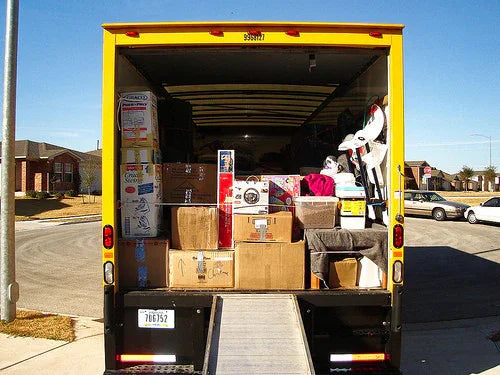 Yellow moving truck parked in a residential area with packed boxes and household items inside